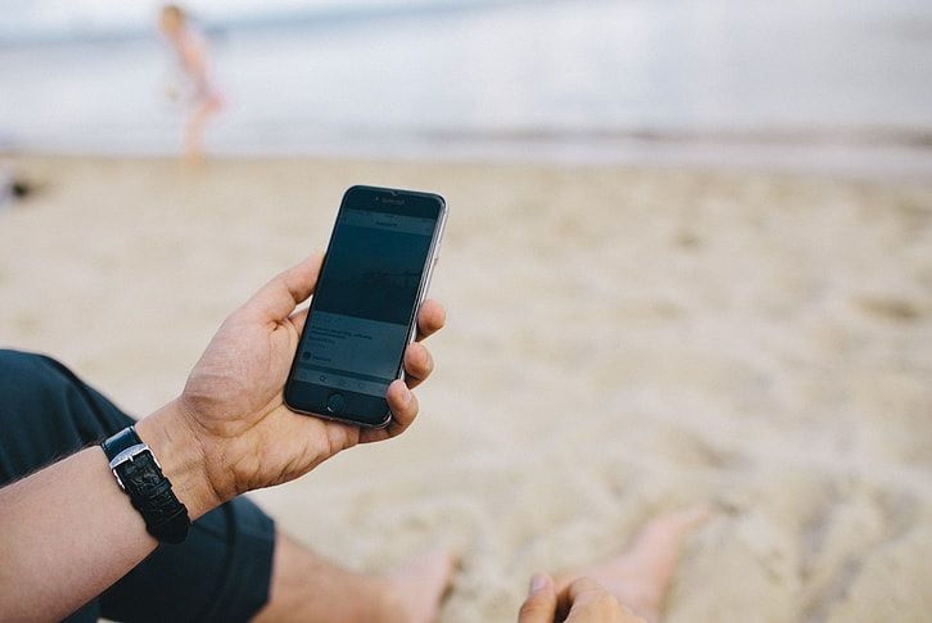 Telefon w dłoni mężczyzny siedzącego na plaży.