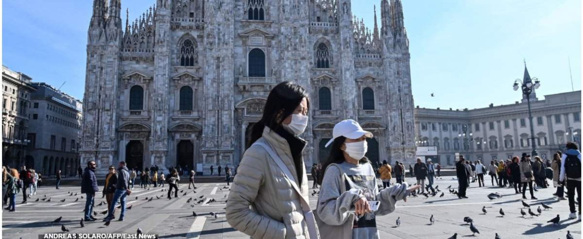 TOPSHOT - Two women wearing a protective facemask walk across the Piazza del Duomo, in front of the Duomo, in central Milan, on February 24, 2020 closed following security measures taken in northern Italy against the COVID-19 the novel coronavirus. - Ital