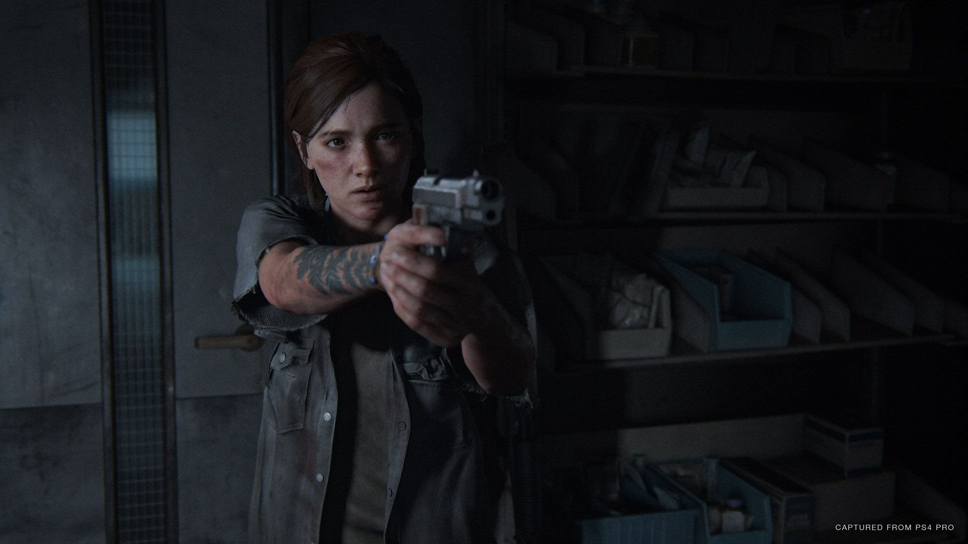 Screen z gry The Last of US Part Two. Główna bohaterka celuje z broni w ciemnym pomieszczeniu.