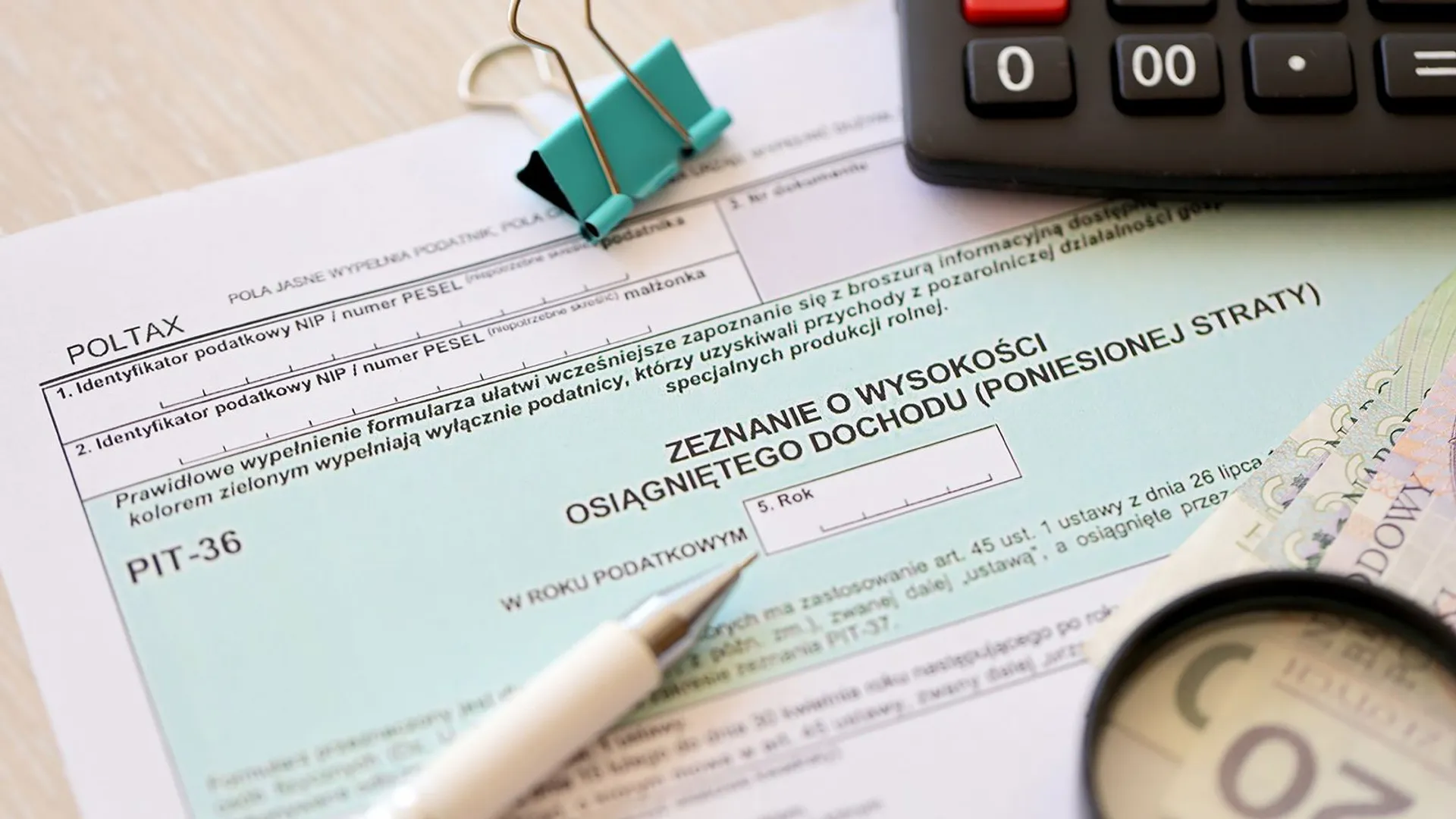 Deklaracja wysokości osiągniętego dochodu lub poniesionej straty - formularze podatkowe PIT-36 na biurku księgowego, obok długopis i polskie banknoty złotowe w zbliżeniu.
