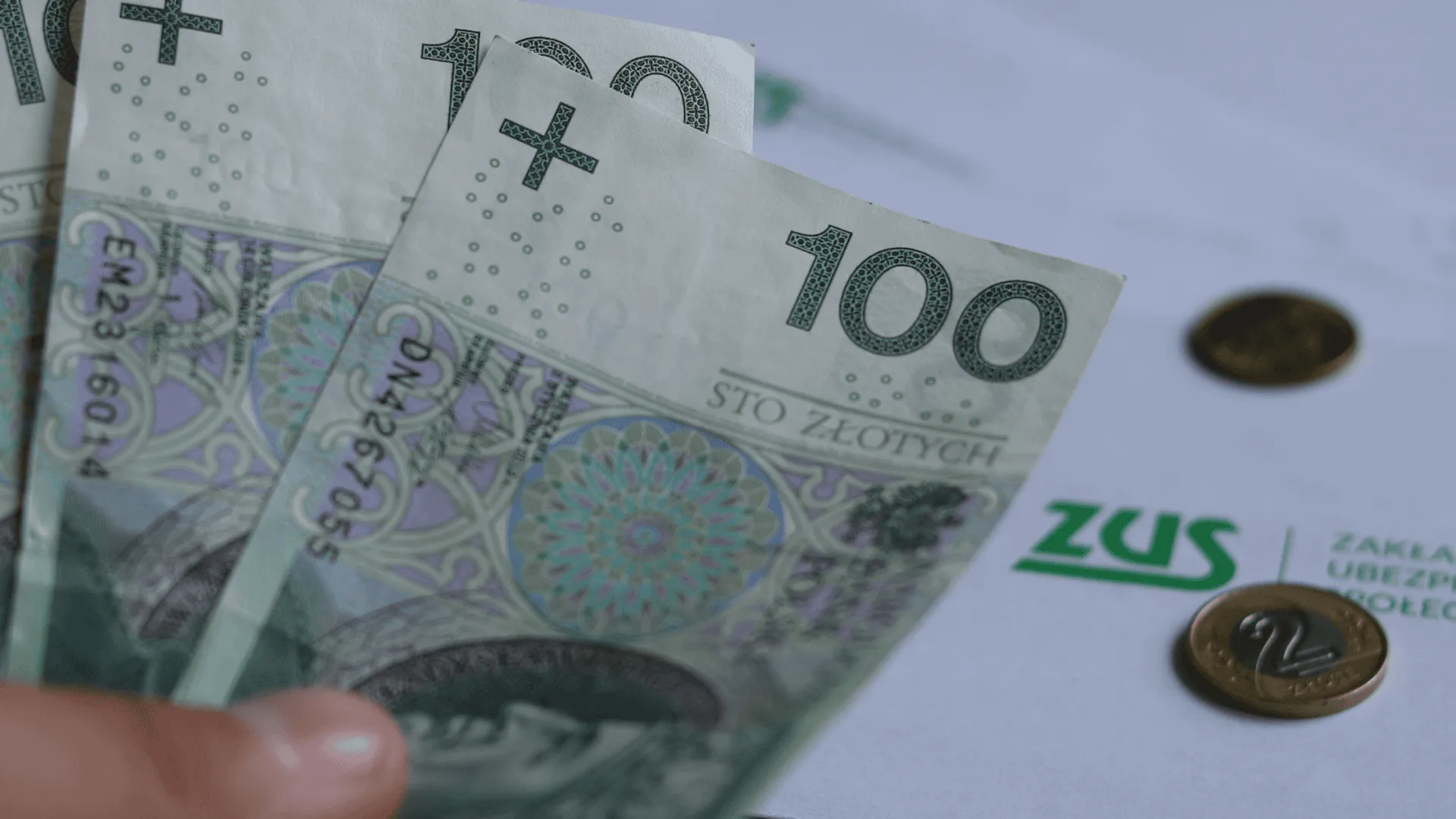 Trzy banknoty o wartości 100 zł, w tle koperta z napisem ZUS