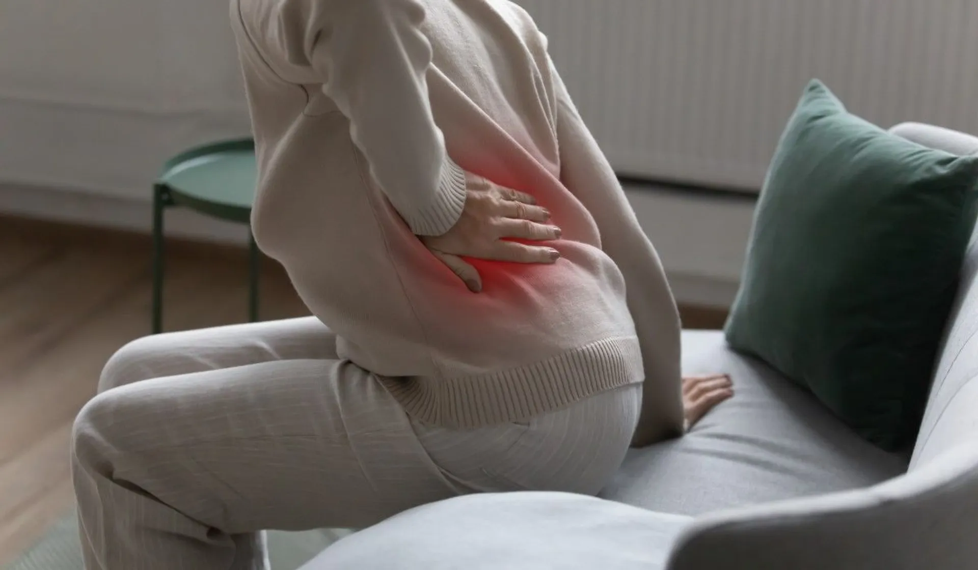 Kobieta trzyma się za plecy przy wstawaniu z kanapy