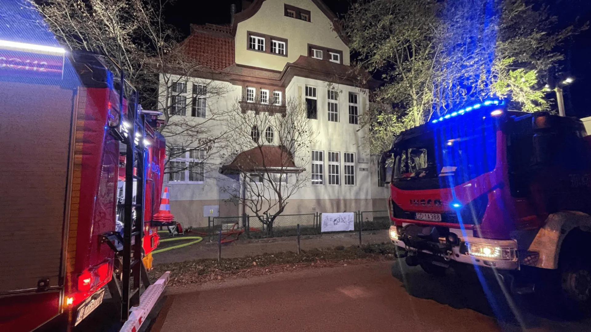 Wozy straży pożarnej stojące przed budynkiem podczas nocnej interwencji.