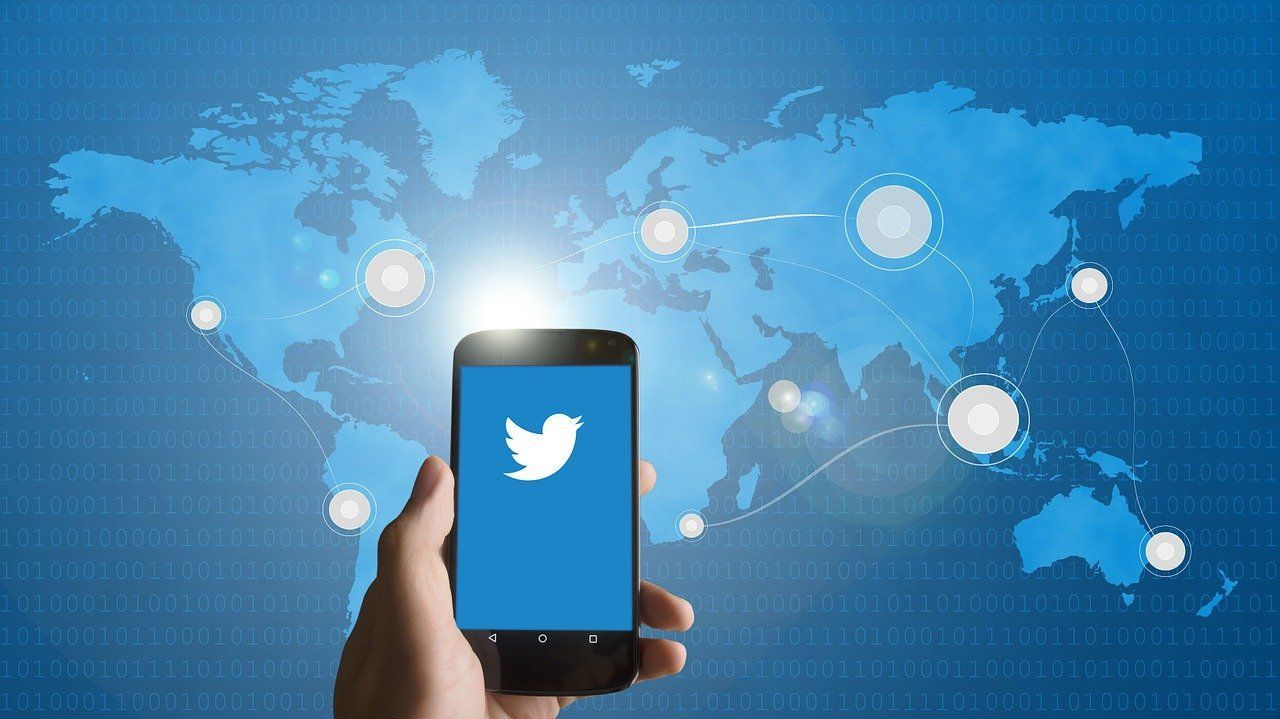 Telefon z logo Twittera trzymany w dłoni na tle niebieskiej mapy świata