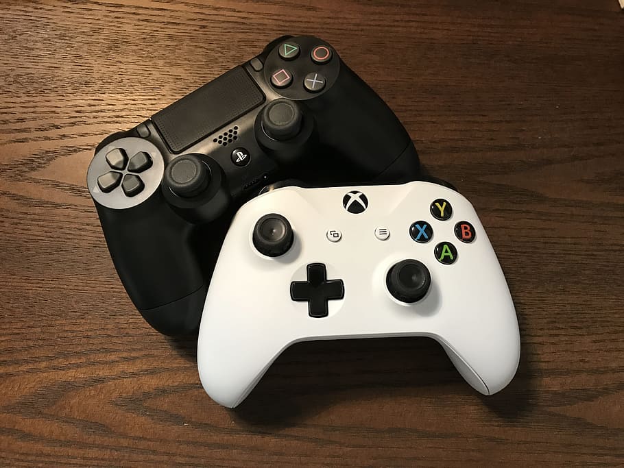 Dwa kontrolery do gier. Niżej biały kontroler do konsoli Xbox One, wyżej czarny pad Dualshock do konsoli PlayStation 4.