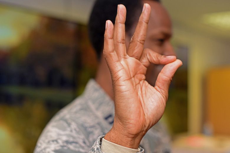 Nauczyciel języka migowego pokazuje znak z tego języka. Czarnoskóry żołnierz, fokus na dłoń.