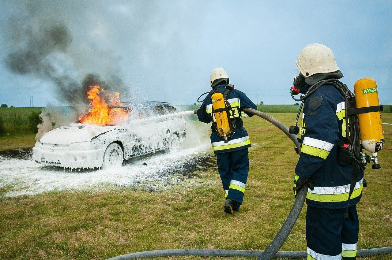 Akcja pożarnicza. StrażPożarna gasi płonący samochód pianą gaśniczą.