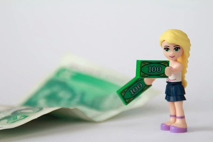 Figurka dziewczynki trzymającej sztuczne pieniądze, w tle banknot.