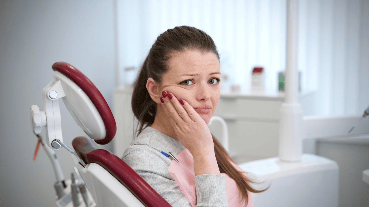 Kobieta u dentysty, trzyma się za policzek, ból zęba