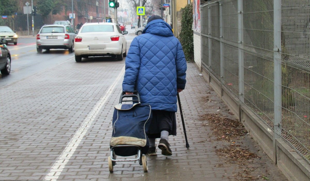Starsza kobieta ciągnąca wózek z zakupami