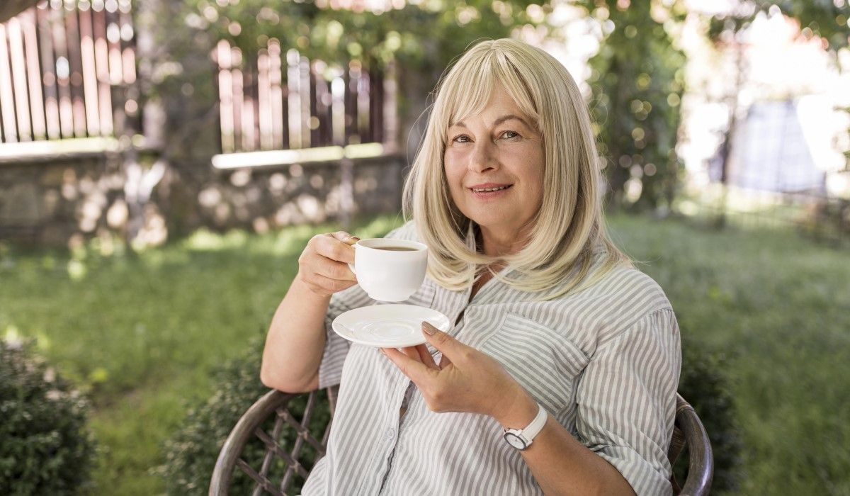 Zadowolona kobieta w średnim wieku pije w ogrodzie kawę