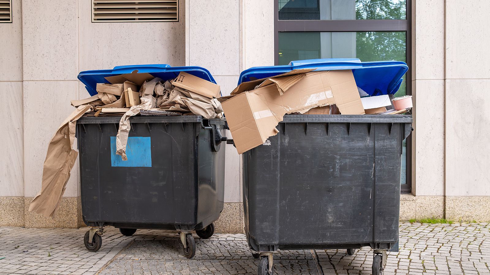 Przepełnione kosze do recyklingu papieru z odpadami kartonowymi przed budynkiem biurowym