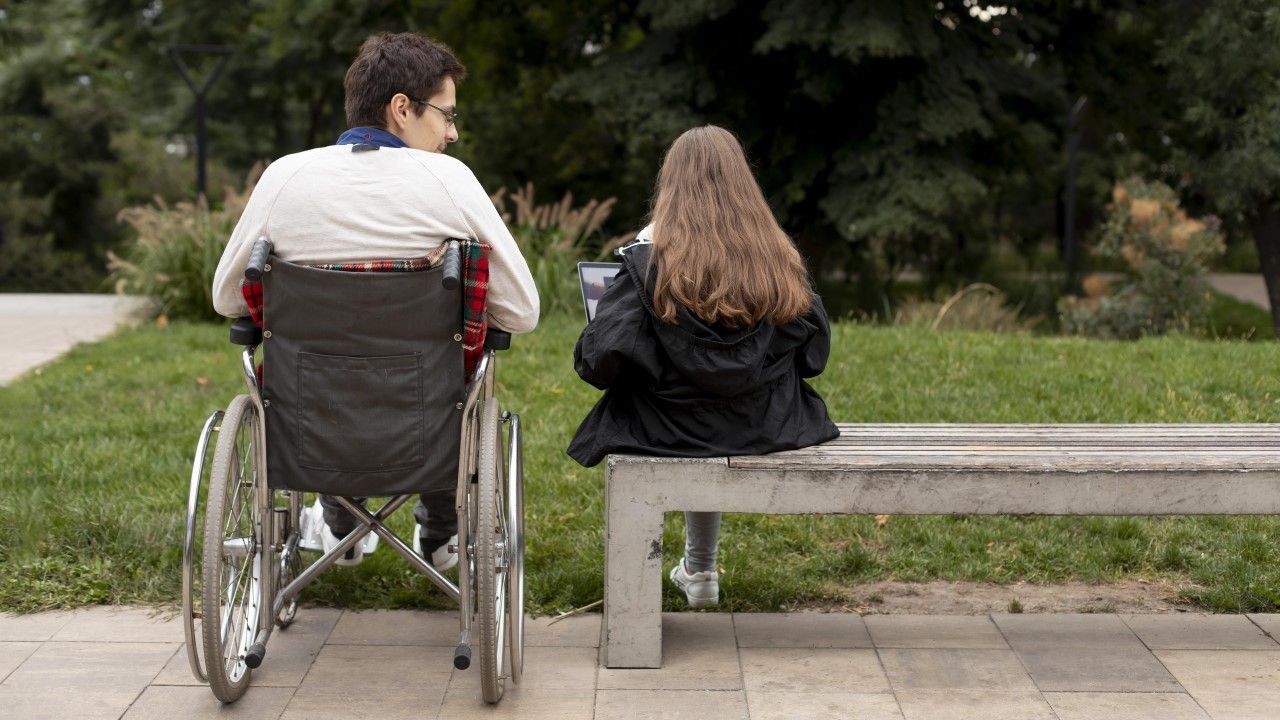 Niepełnosprawny mężczyzna na wózku inwalidzkim w parku, obok na ławce córka