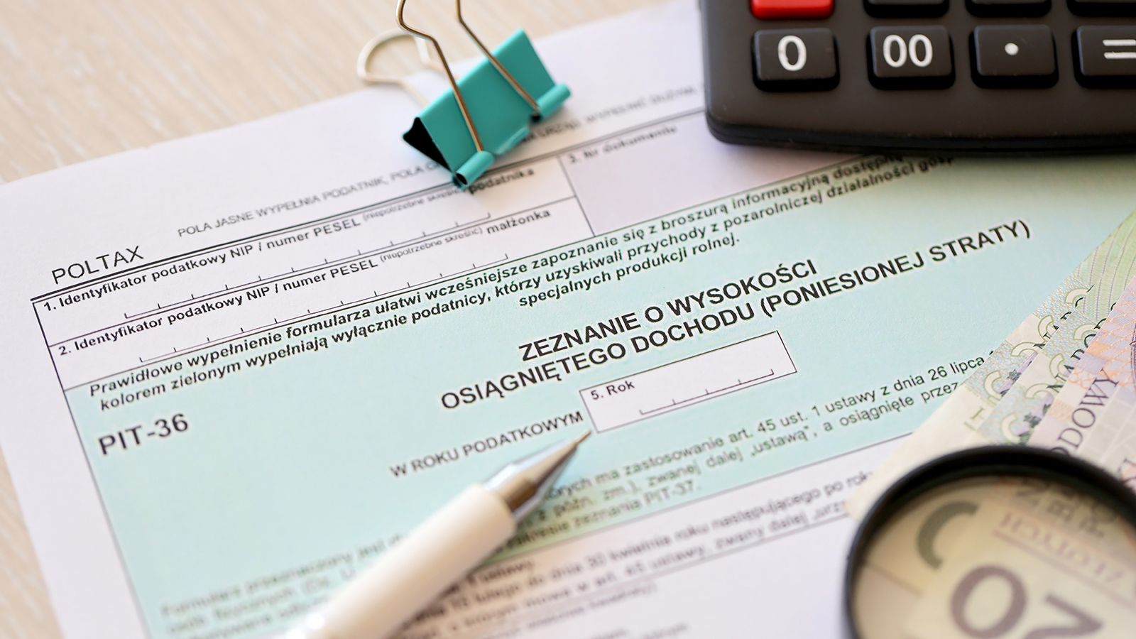 Deklaracja wysokości osiągniętego dochodu lub poniesionej straty - formularze podatkowe PIT-36 na biurku księgowego, obok długopis i polskie banknoty złotowe w zbliżeniu.