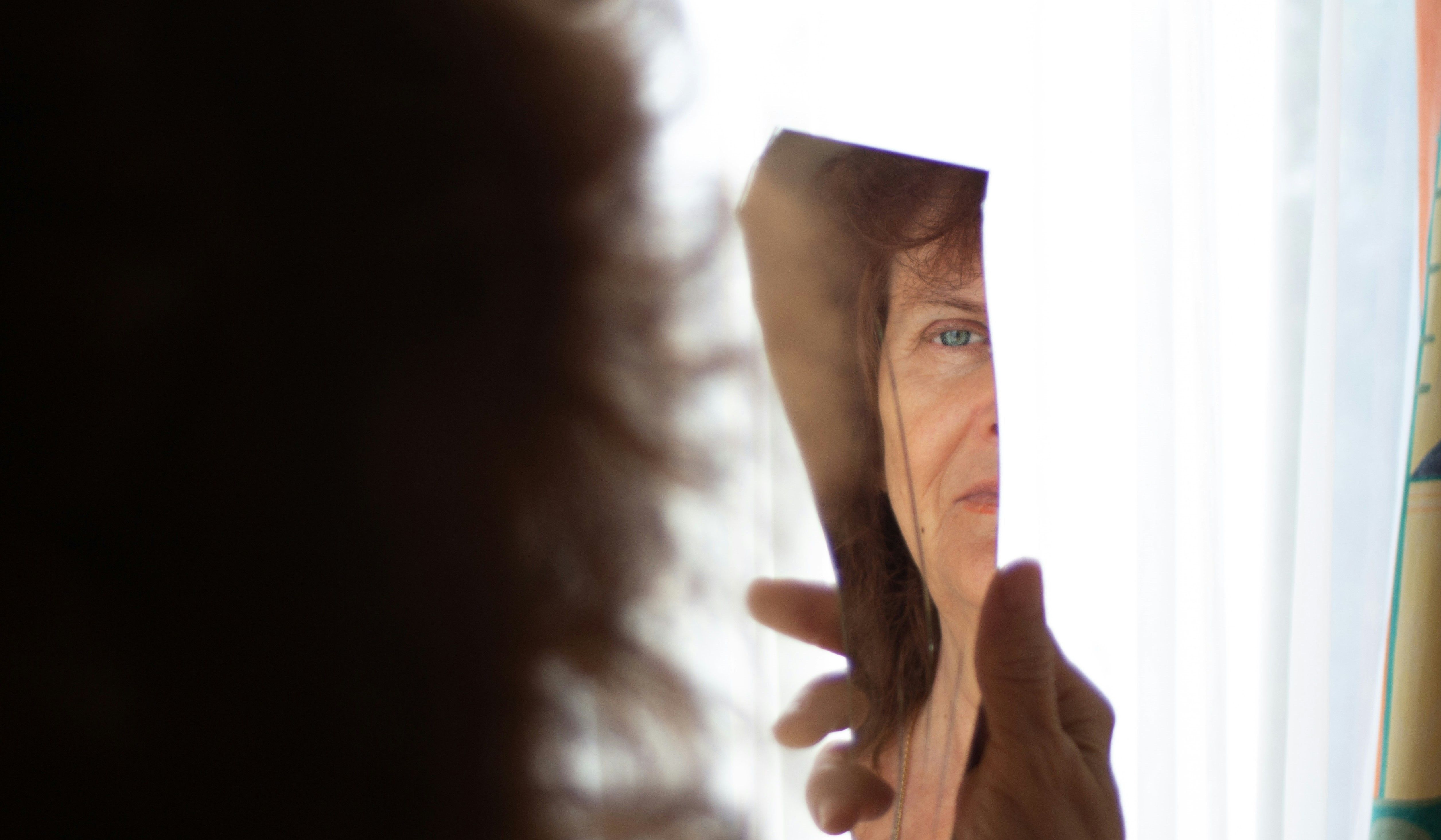 Kobieta przygląda się swojemu oku w potłuczonym lustrze
