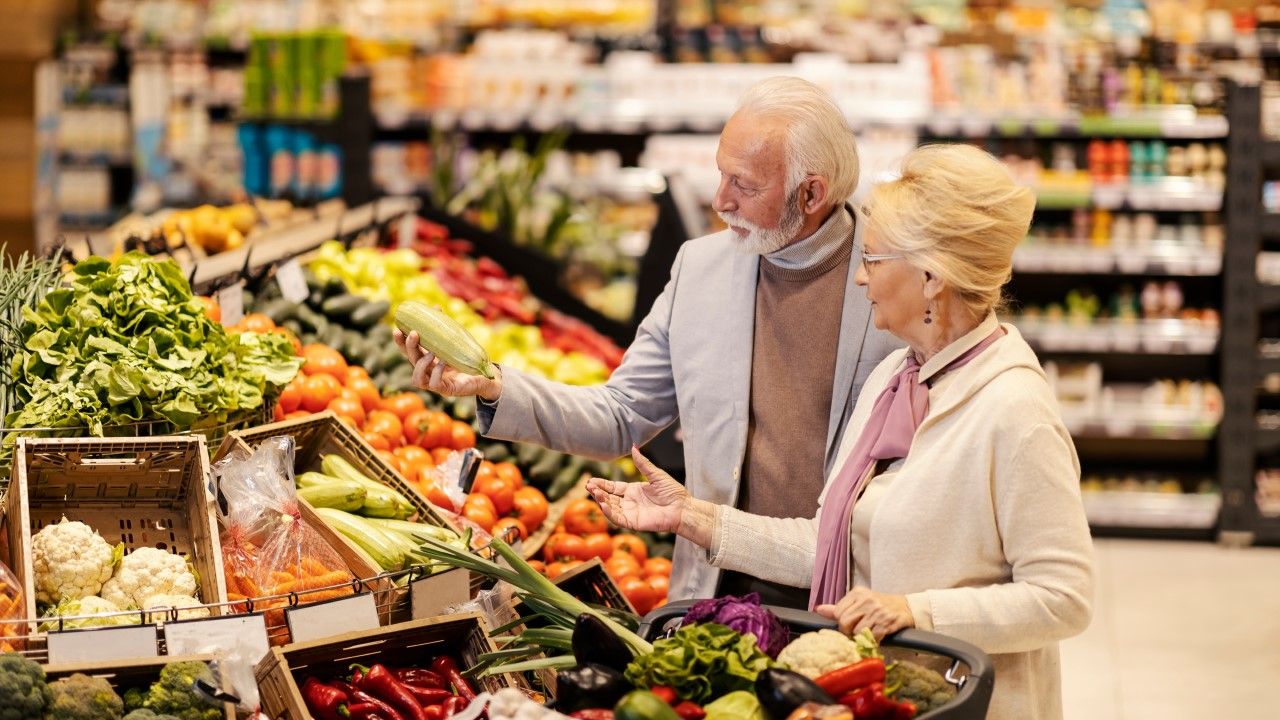 Seniorzy na zakupach w markecie wybierają warzywa