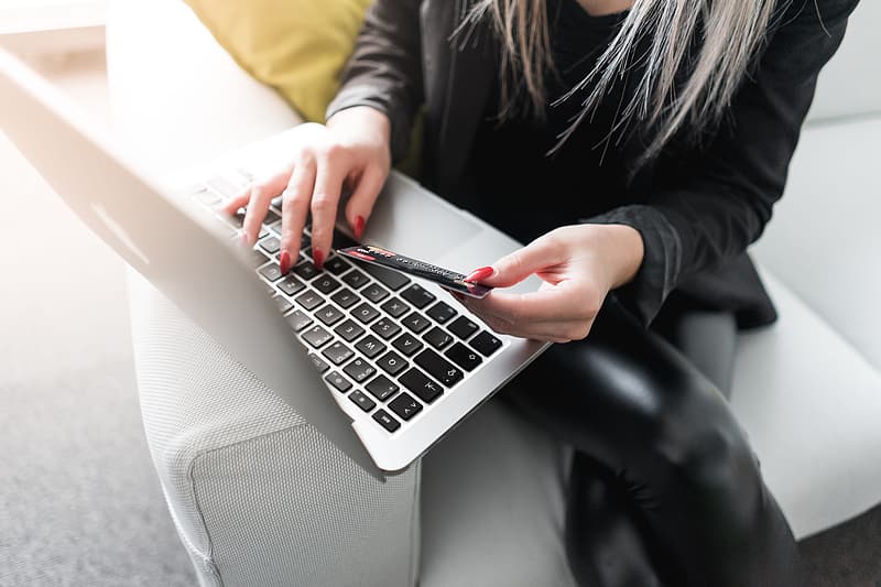 Kobieta wpisująca dane z karty kredytowej do laptopa. czerwone paznokcie, skóra, apple.
